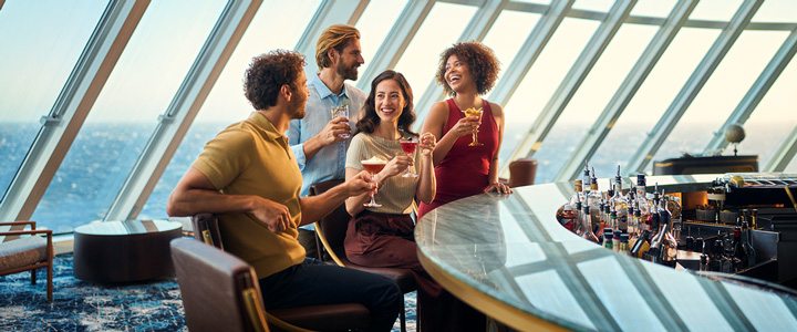 An der Bar der Mein Schiff Flow genießen fröhliche Urlaubsgäste Cocktails, während durch große Glasfronten der Blick auf das weite Meer fällt.