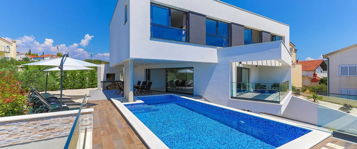 Ein moderner weißer Bau mit großen Glasfronten in Kroatien. Vor der Anlage erstreckt sich ein strahlend blauer, großzügiger Pool im klaren Sonnenlicht.